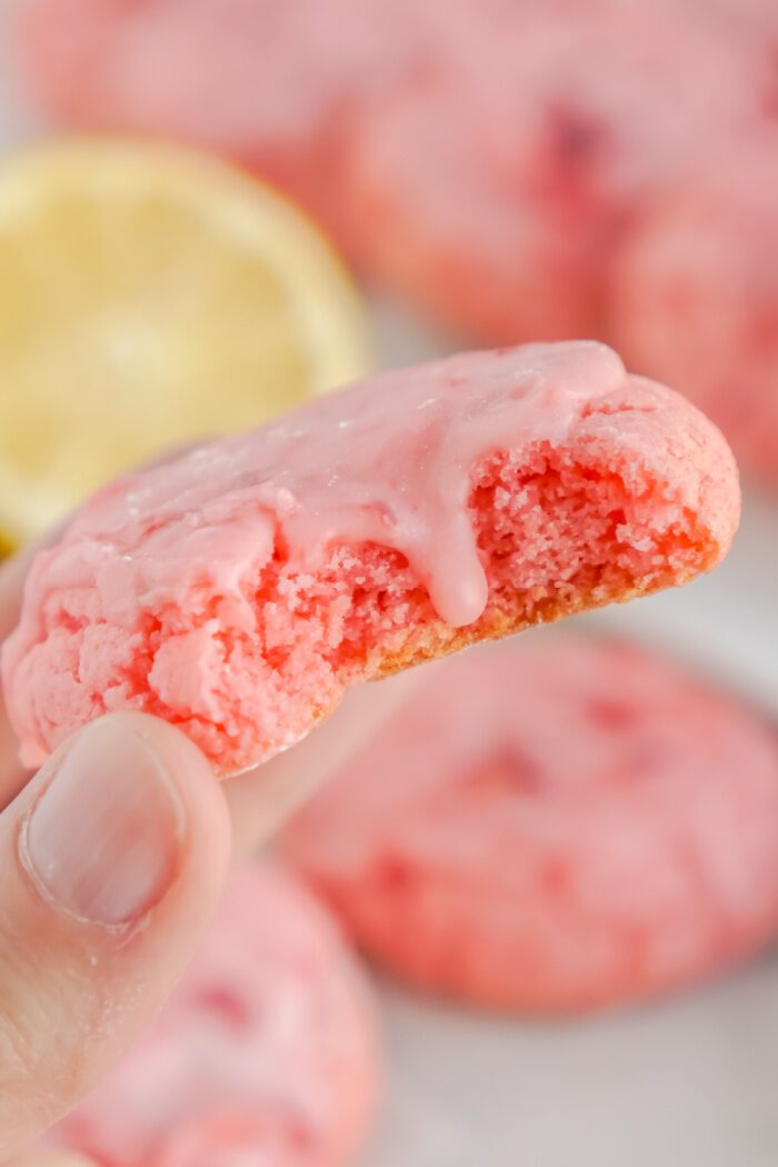 Someone holding a strawberry cake mix cookie with a bite taken out of it