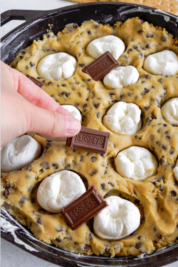 Adding marshmallows and hershey chocolate on top of cookie dough