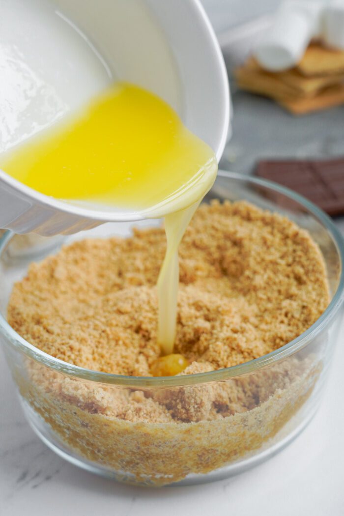 Butter being poured into crushed graham crackers