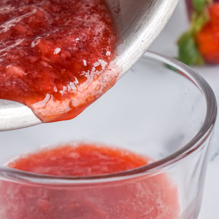 Strawberry sauce being poured from a saucepan.