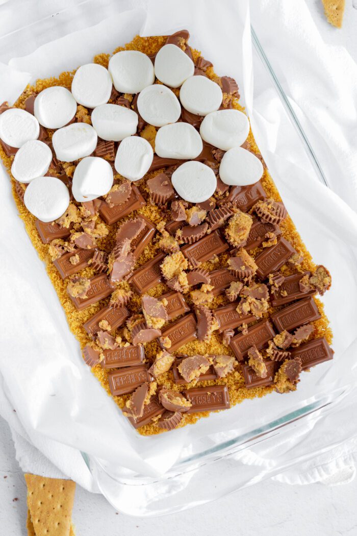 Adding s'mores, peanut butter cups, and hershey's chocolate on top of graham cracker crust