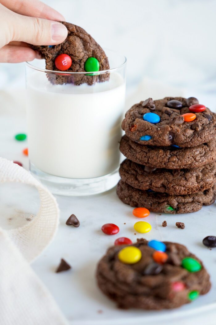 Someone dipping a M&M Cookie in a glass of milk