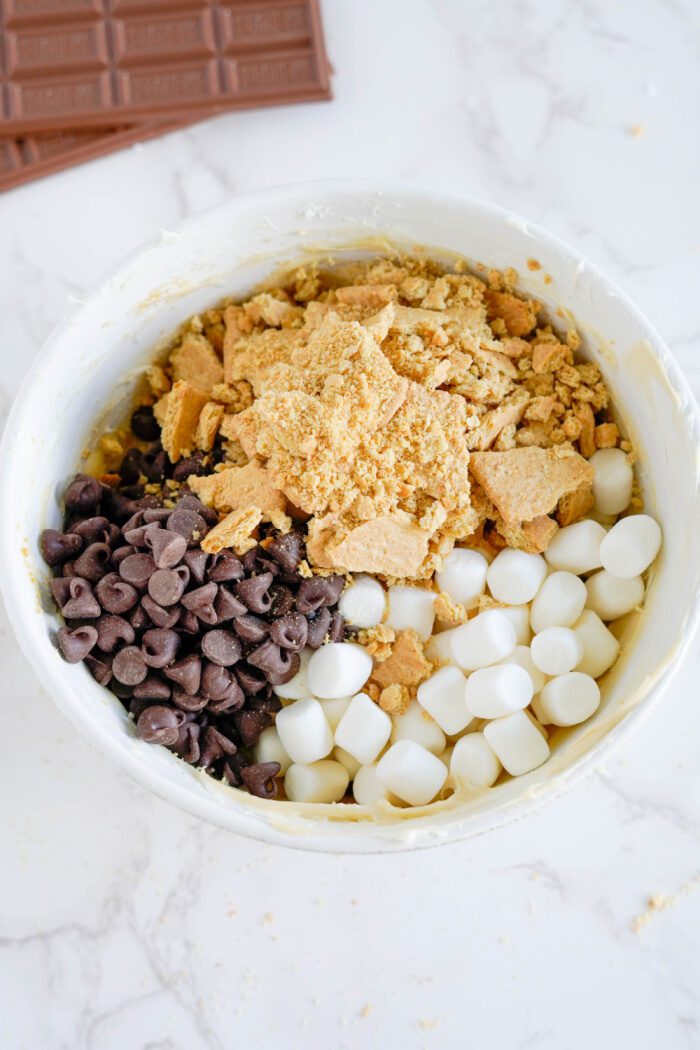 Graham crackers, marshmallows, and chocolate chips being added to the bowl