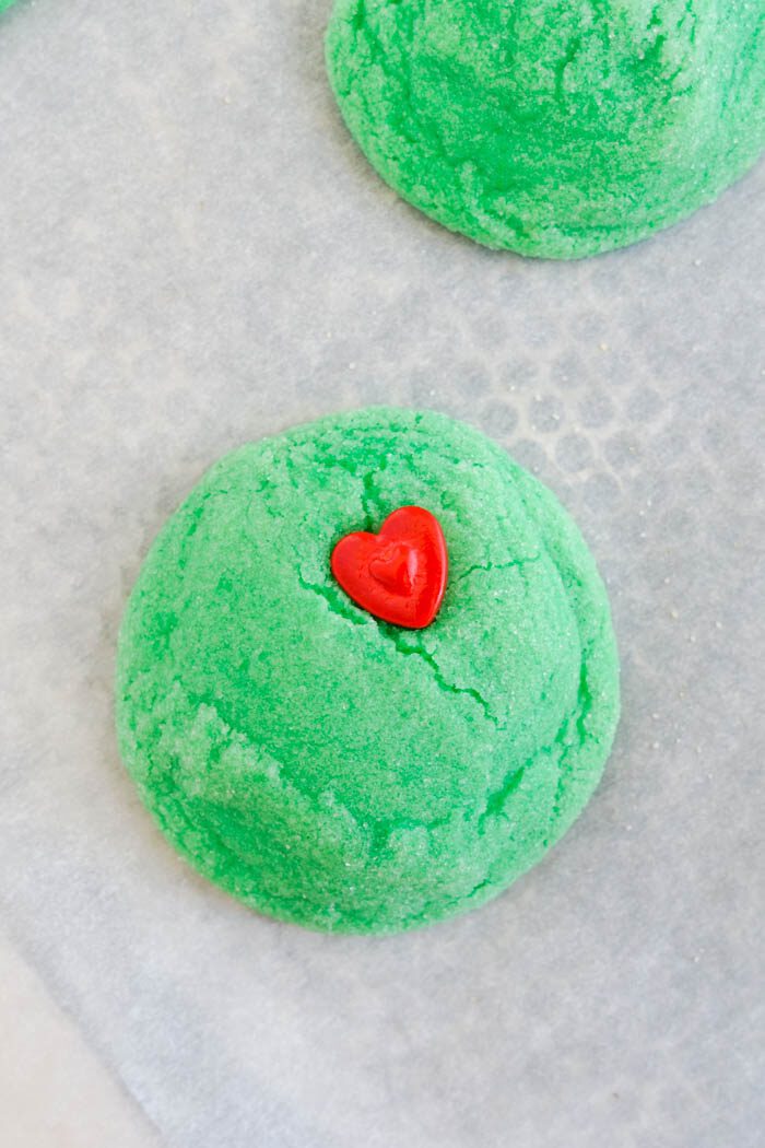 A green sugar cookie with a red heart on top.