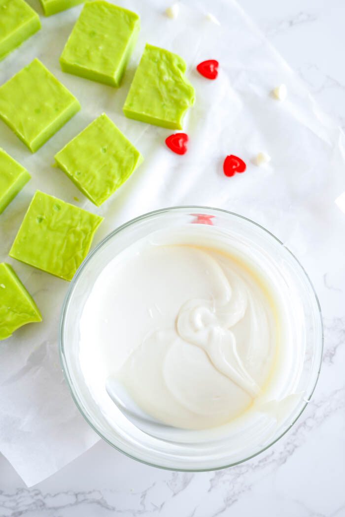 A bowl of white chocolate next to green candy.