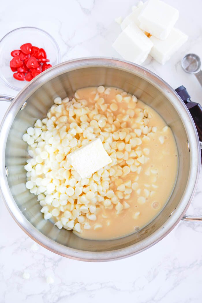 A metal bowl with white chocolate chips, butter, and sweetened condensed milk.