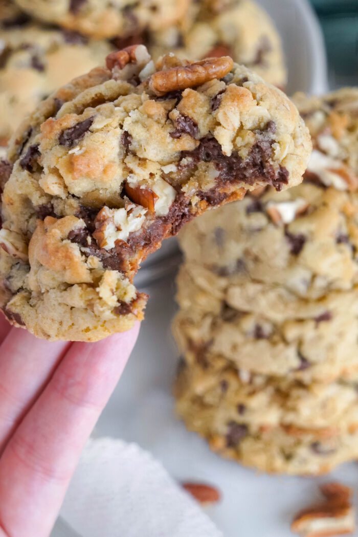 A hand holding a chocolate chip cookie with pecans.