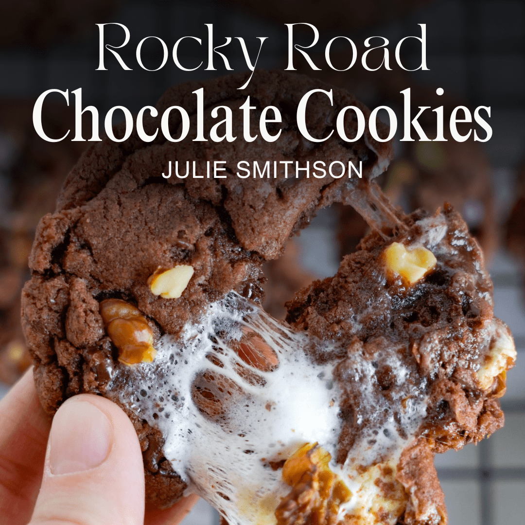 A hand holding a rocky road chocolate cookie with prominently visible marshmallows and nuts. Text overlay reads “Easy Rocky Road Cookies Recipe” by Julie Smithson.