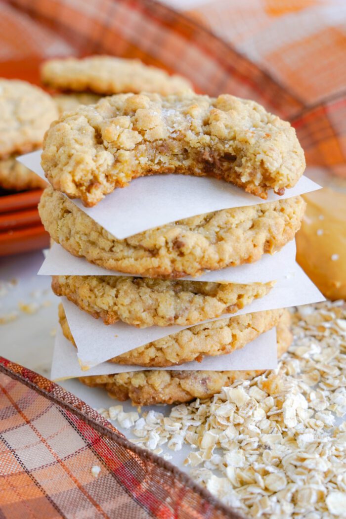 A stack of four oatmeal cookies with a bite taken out of the top cookie.