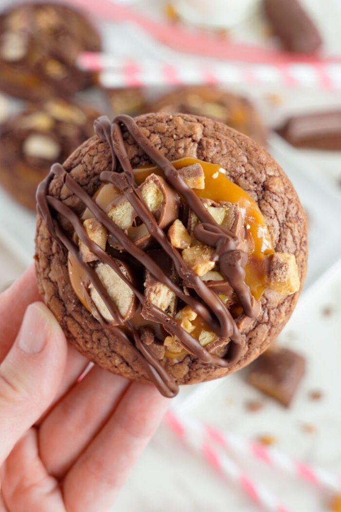 A hand holding a chocolate chip cookie with caramel and candy pieces.