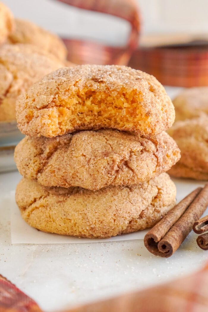 A stack of three pumpkin cookies with cinnamon sticks.