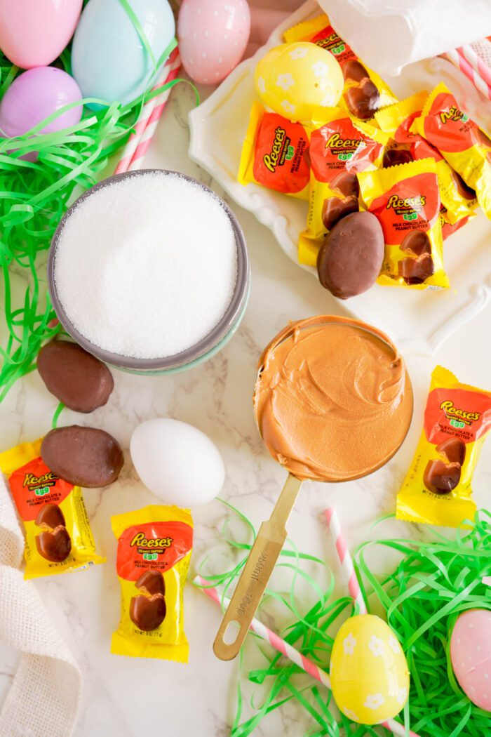 Easter-themed candy arrangement with Reese's Egg Peanut Butter Cookies, plastic eggs, and a spoonful of peanut butter on a marble surface.