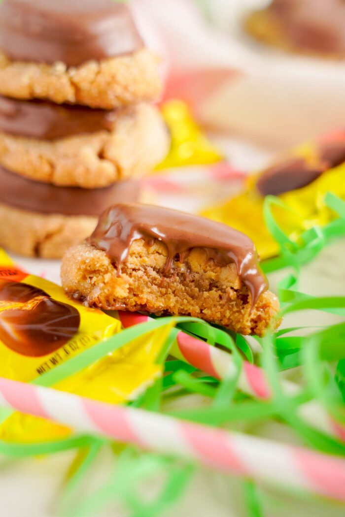 A stack of Reese's Egg Peanut Butter Cookies with colorful candy wrappers in the background.