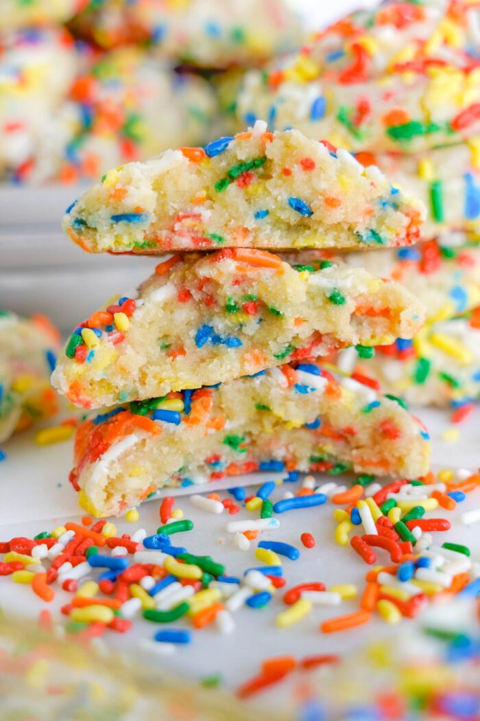 Stack of sprinkle-covered cookies with one broken in half, revealing a soft interior.