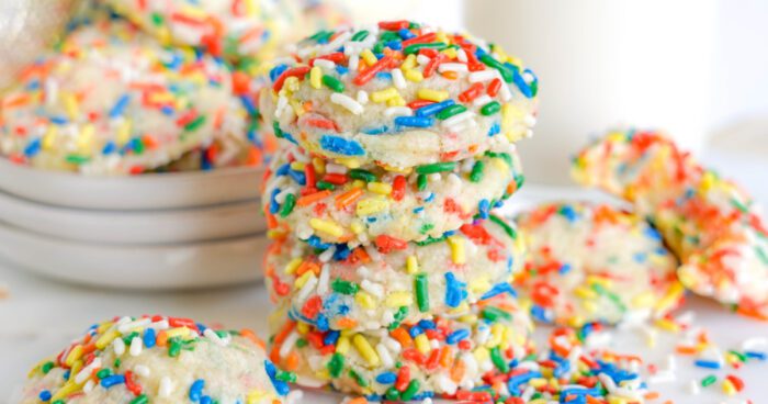 A stack of sprinkle-covered cookies beside a glass of milk.