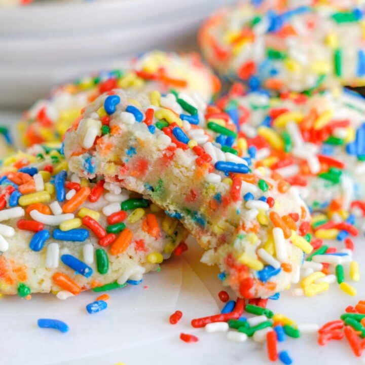 Colorful sprinkle-covered cookies with one bitten into.