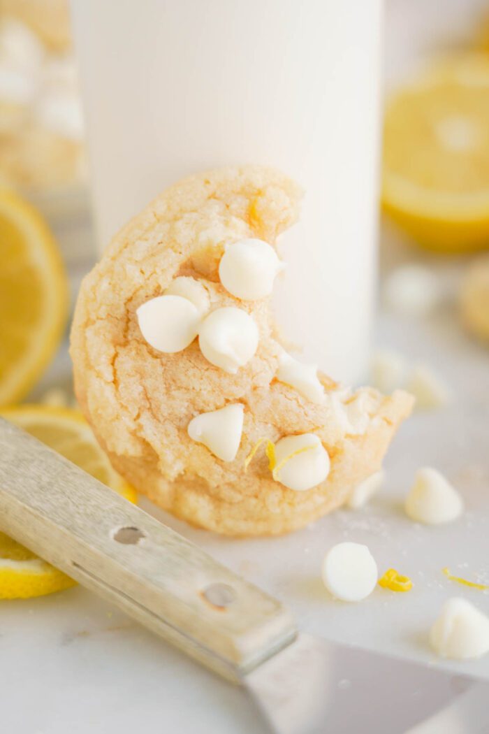A lemon white chocolate chip cookie, partially eaten, beside a glass of milk.