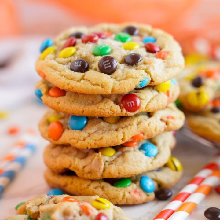 A stack of the best homemade peanut butter cookies with colorful M&M candy pieces on a white surface.