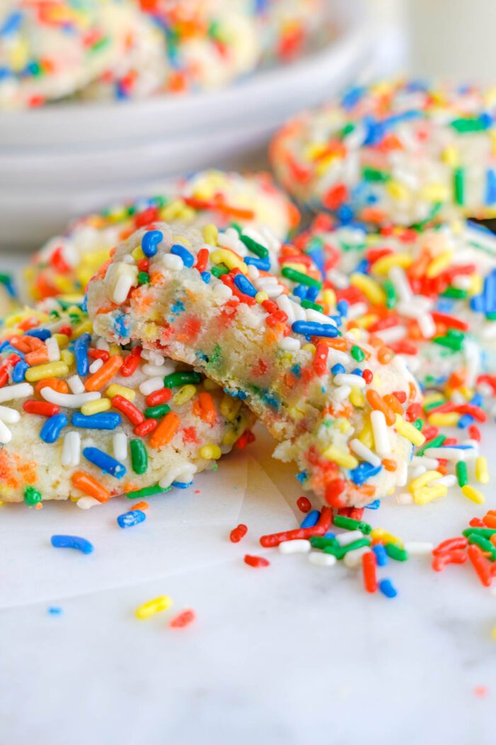 Colorful sprinkle-coated cookies with a bite taken out, displaying a soft texture and vibrant interior.