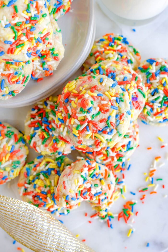 A plate of colorful sprinkle-covered cookies with a glass of milk nearby.