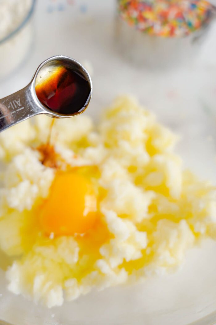 Pouring vanilla extract into a bowl of cookie dough ingredients.