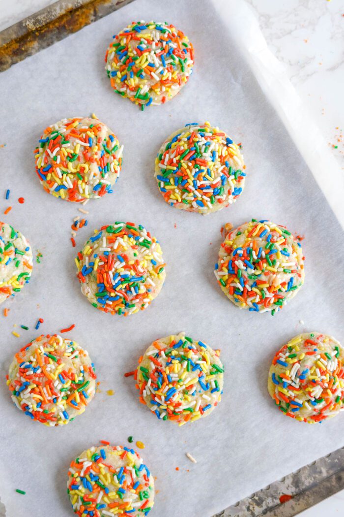 Freshly baked cookies topped with colorful sprinkles on parchment paper.