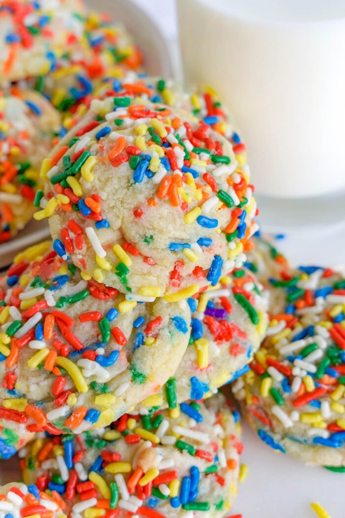 A stack of sprinkle-covered cookies next to a glass of milk.