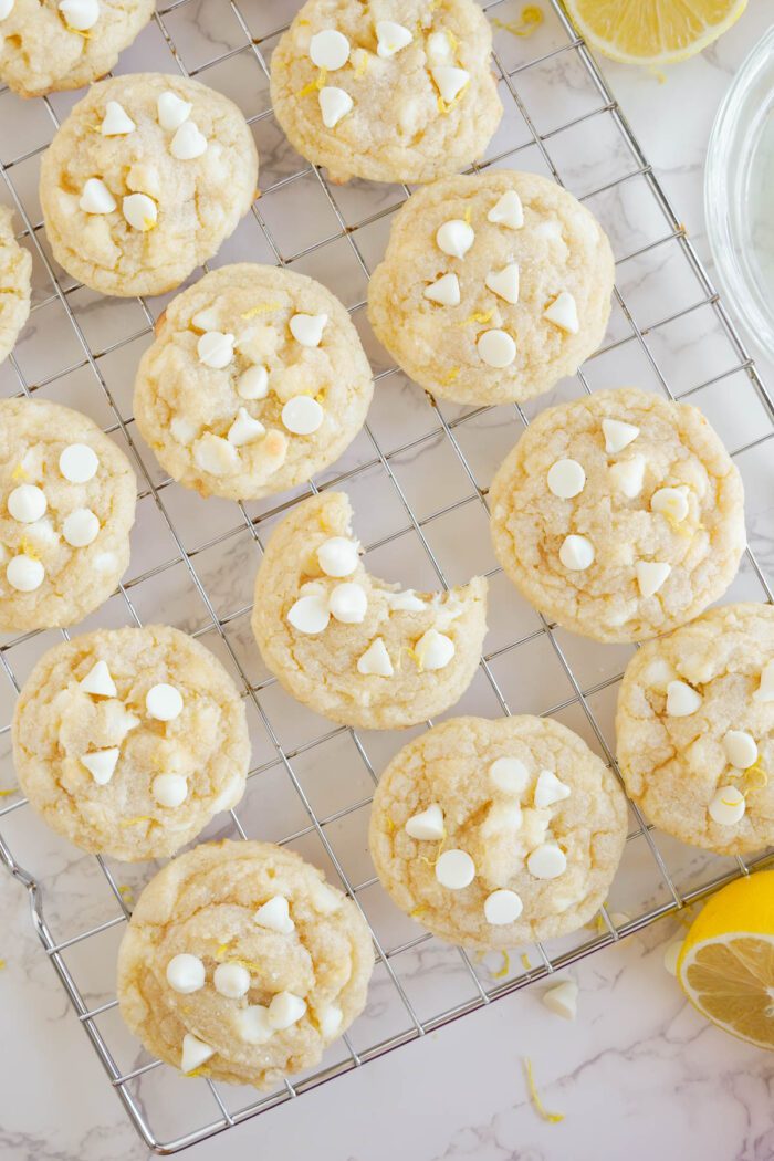 A batch of freshly baked Lemon White Chocolate Chip Cookies cooling on a wire rack.