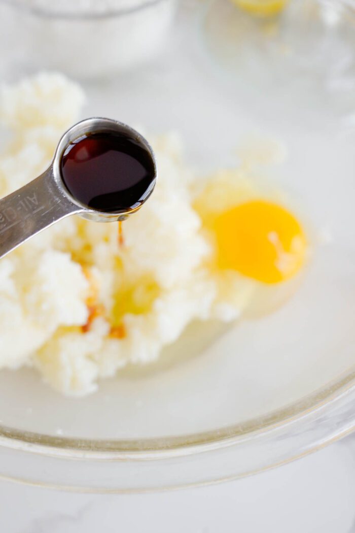 A teaspoon of vanilla extract is added to a bowl.
