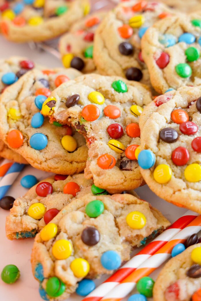 A close-up of colorful peanut butter M&M chocolate chip cookies on a striped surface.