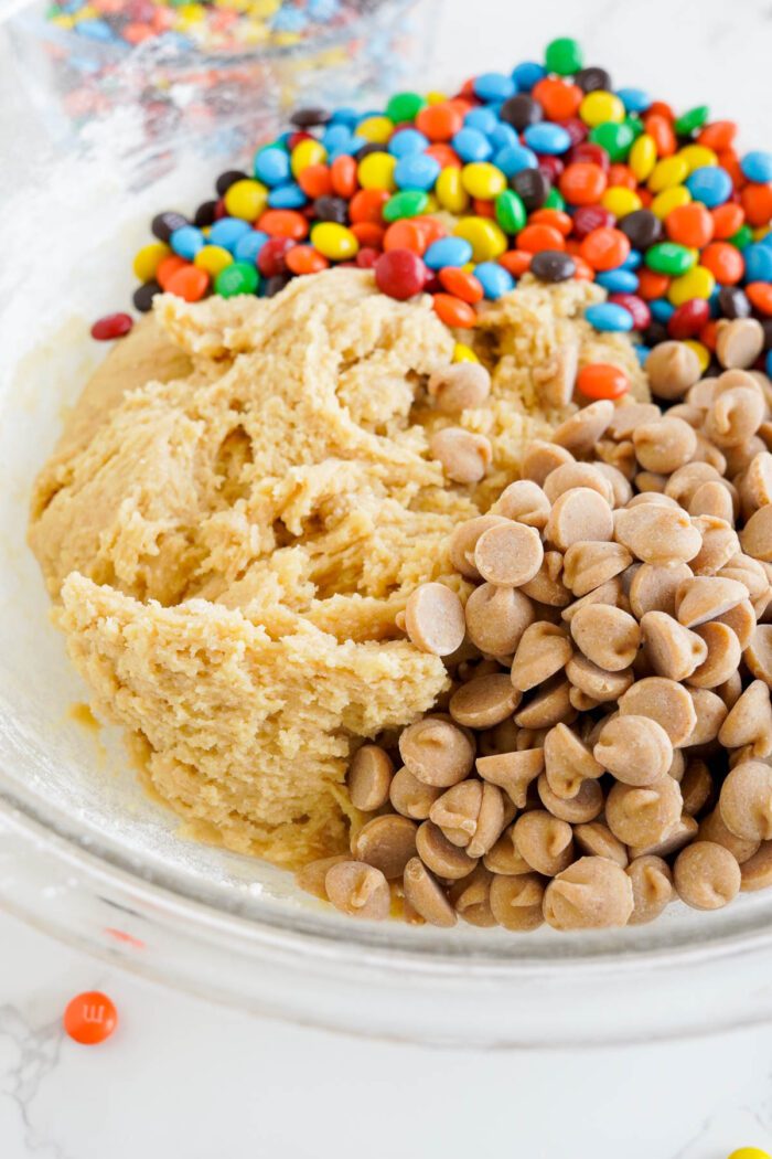 Best cookie dough in a mixing bowl with chocolate chips and colorful peanut butter M&M pieces on the side.