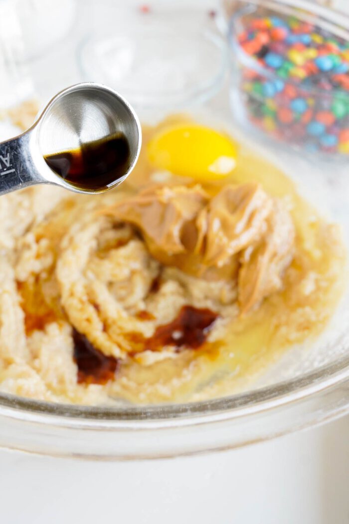 Best Vanilla extract being poured into a mixing bowl with peanut butter M&M cookie ingredients.