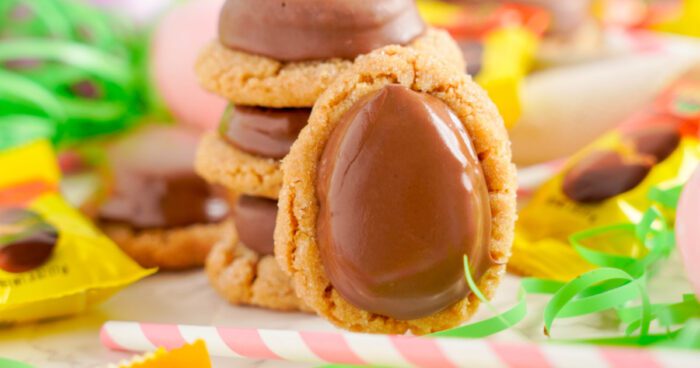 Cookies topped with Reese's Egg Peanut Butter candies, surrounded by colorful candy wrappers.