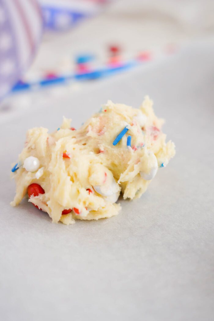 A scoop of colorful, sprinkle-infused cookie dough for easy 4th of July cookies on parchment paper.