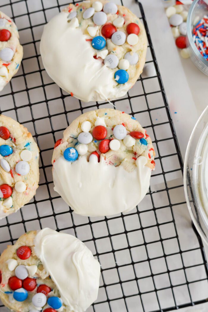 Cookies topped with white chocolate and colorful candy pieces, cooling on a wire rack, ideal for an easy 4th of July treat.