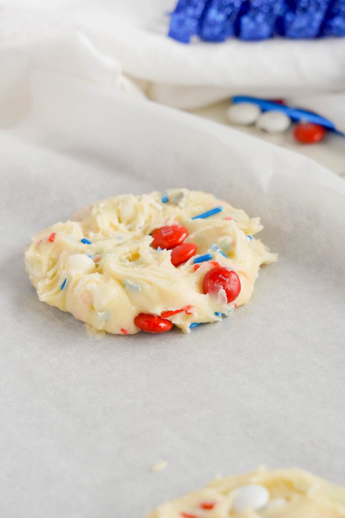 Unbaked cookie dough with red and blue candies on parchment paper, easy 4th of July cake mix cookies in the background.