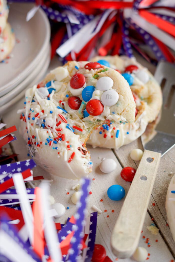 An easy 4th of July cake mix cookie with red, white, and blue sprinkles and M&M's, surrounded by patriotic ribbons and decorations.