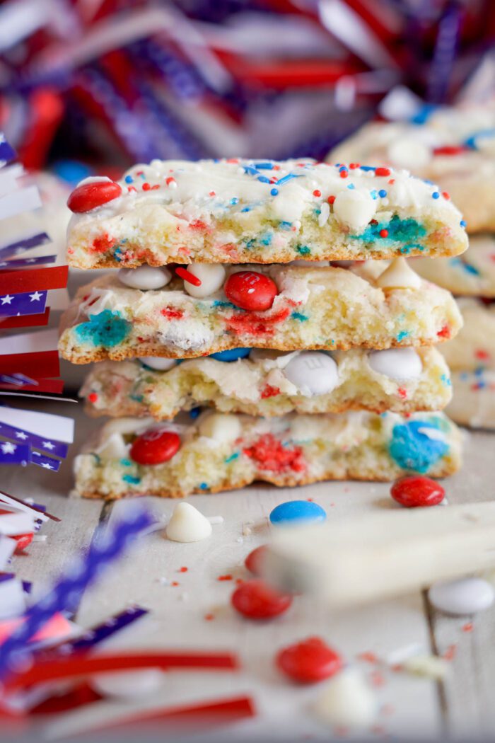 Stack of patriotic-themed cookies with red, blue, and white candy pieces, perfect as Easy 4th of July Cake Mix Cookies, surrounded by American flag decorations.