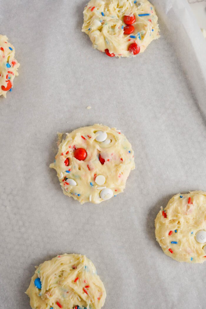 Easy unbaked cookies with colorful sprinkles on parchment paper, spaced evenly apart.
