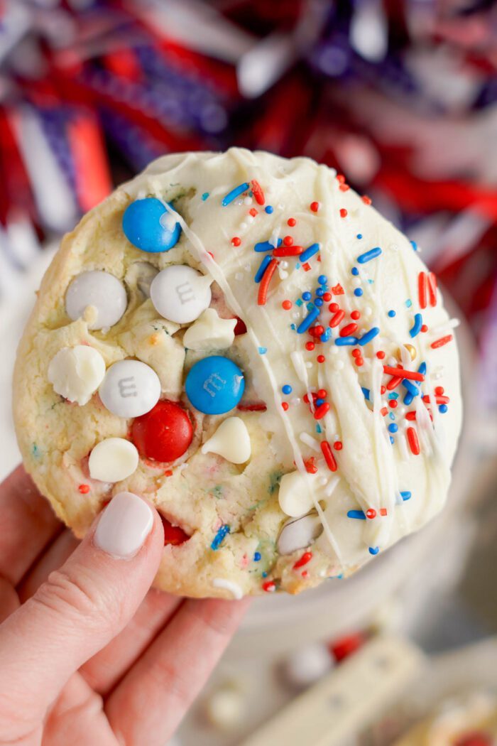 A close-up of a hand holding an easy 4th of July cookie with red, white, and blue m&m's, white chocolate chips, and sprinkles.