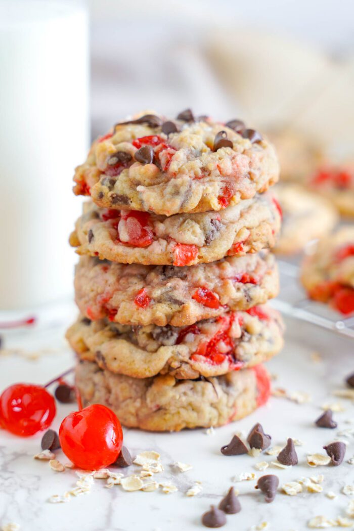 A Cherry Chocolate Chip Cookies Recipe featuring a stack of cookies with red candied cherries and chocolate chips, accompanied by a glass of milk.
