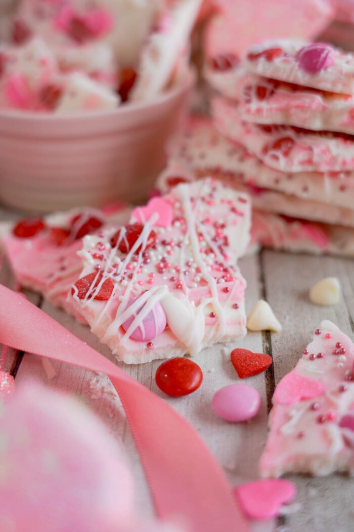 White chocolate candy bark with sprinkles and candy hearts, displayed on a wooden surface with a pink ribbon.