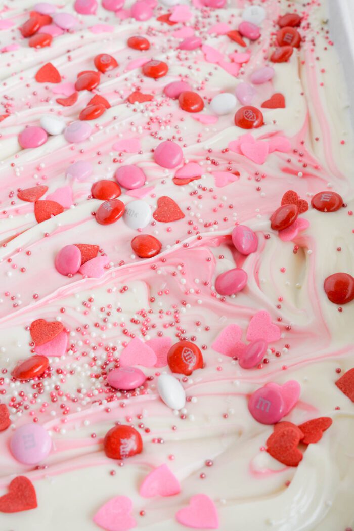 White chocolate bark topped with pink swirls and an assortment of valentine's day-themed candies and sprinkles.