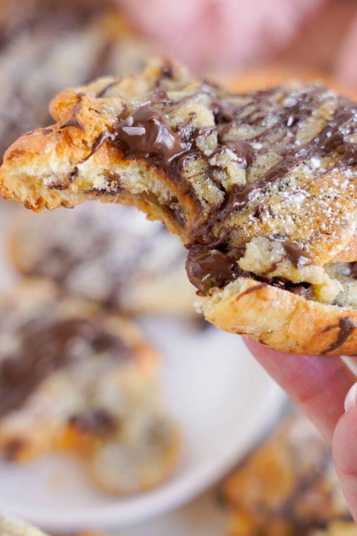 A close-up photo of a hand holding a chocolate-stuffed croissant, torn in half to reveal a gooey chocolate and nut filling.