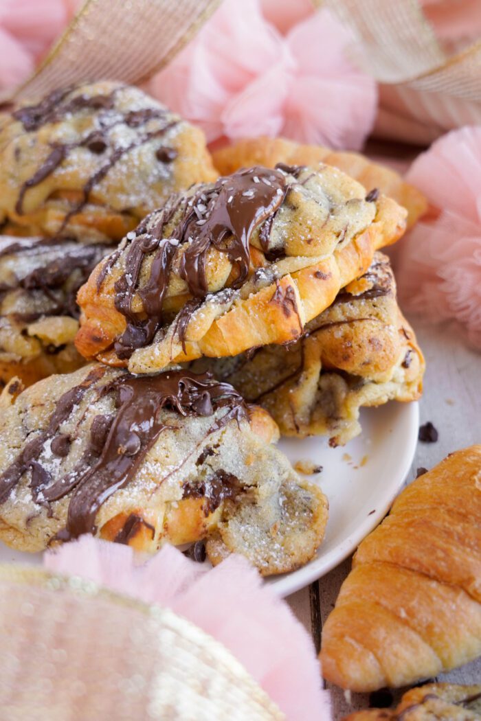 Plate of freshly baked chocolate chip cookie croissants with powdered sugar, surrounded by pink decorations.