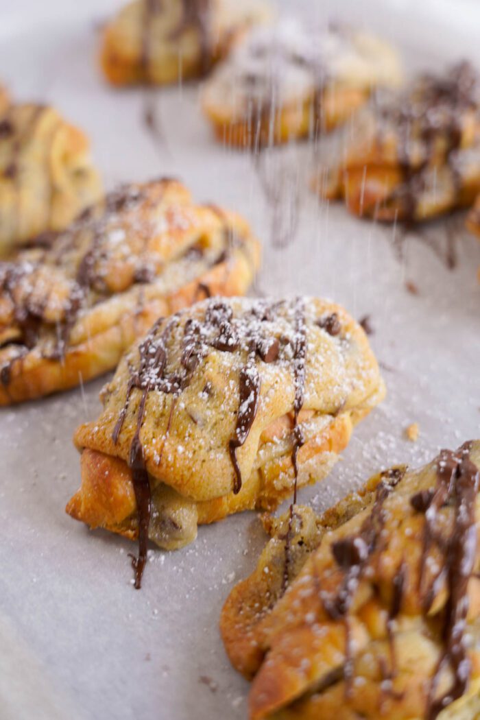 Freshly baked chocolate chip croissants with almond topping on parchment paper.