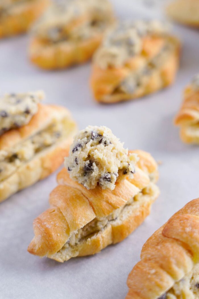 Close-up of croissants stuffed with chocolate chip cookie dough, displayed on a light background.