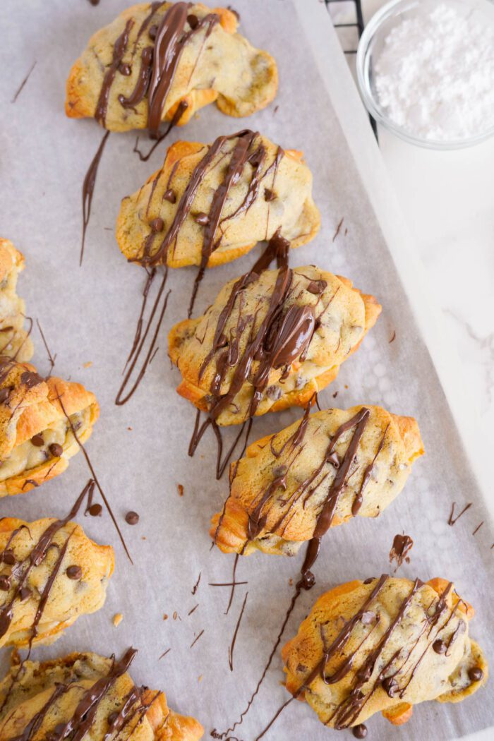Chocolate drizzled crescent cookies on parchment paper.