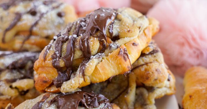 Close-up of a chocolate drizzled croissant with powdered sugar on a plate.