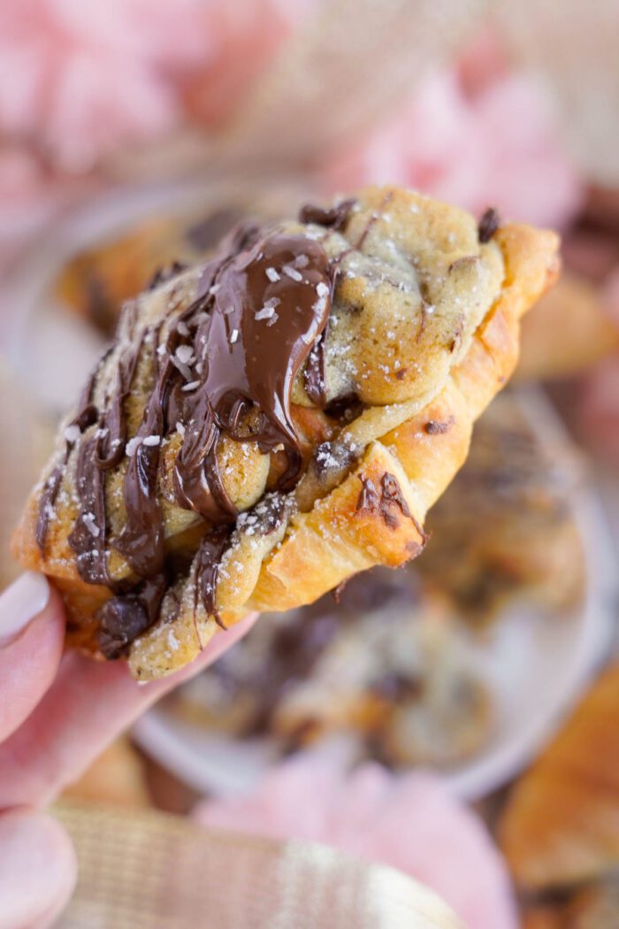 A close-up of a hand holding a chocolate chip cookie topped with nuts.